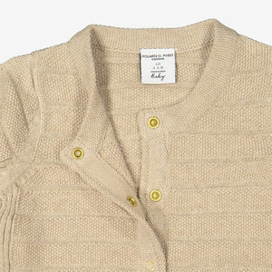 Close up of unisex beige knitted cardigan in 100% organic cotton showing easy popper fastening. 