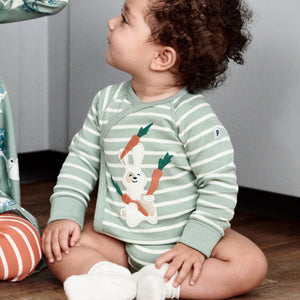 A toddler wearing a green and white striped cotton long sleeve babygrow with fun bunny eating carrots applique, paired with white organic cotton socks