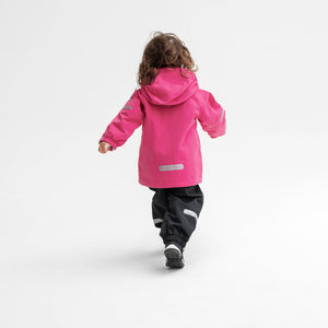 Back view of a girl wearing a pink, kids waterproof jacket paired with black, kids waterproof trousers, made of shell fabric.