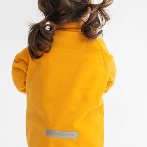 Back view of a young girl wearing a yellow, kids waterproof fleece jacket with cuff thumbholes, made of lightweight fabric.