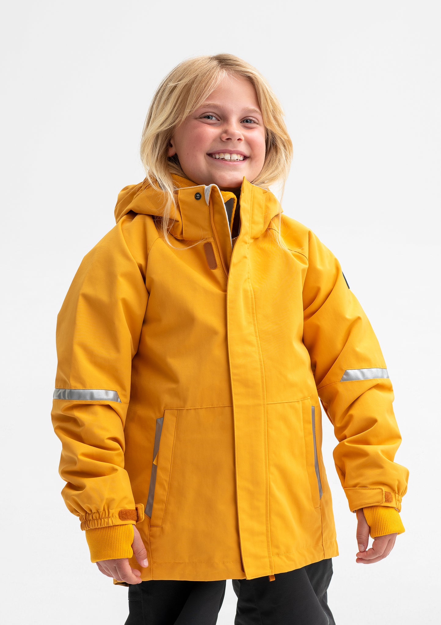 A young girl wearing a yellow waterproof jacket for kids, includes a detachable hood, front pockets and reflectors.