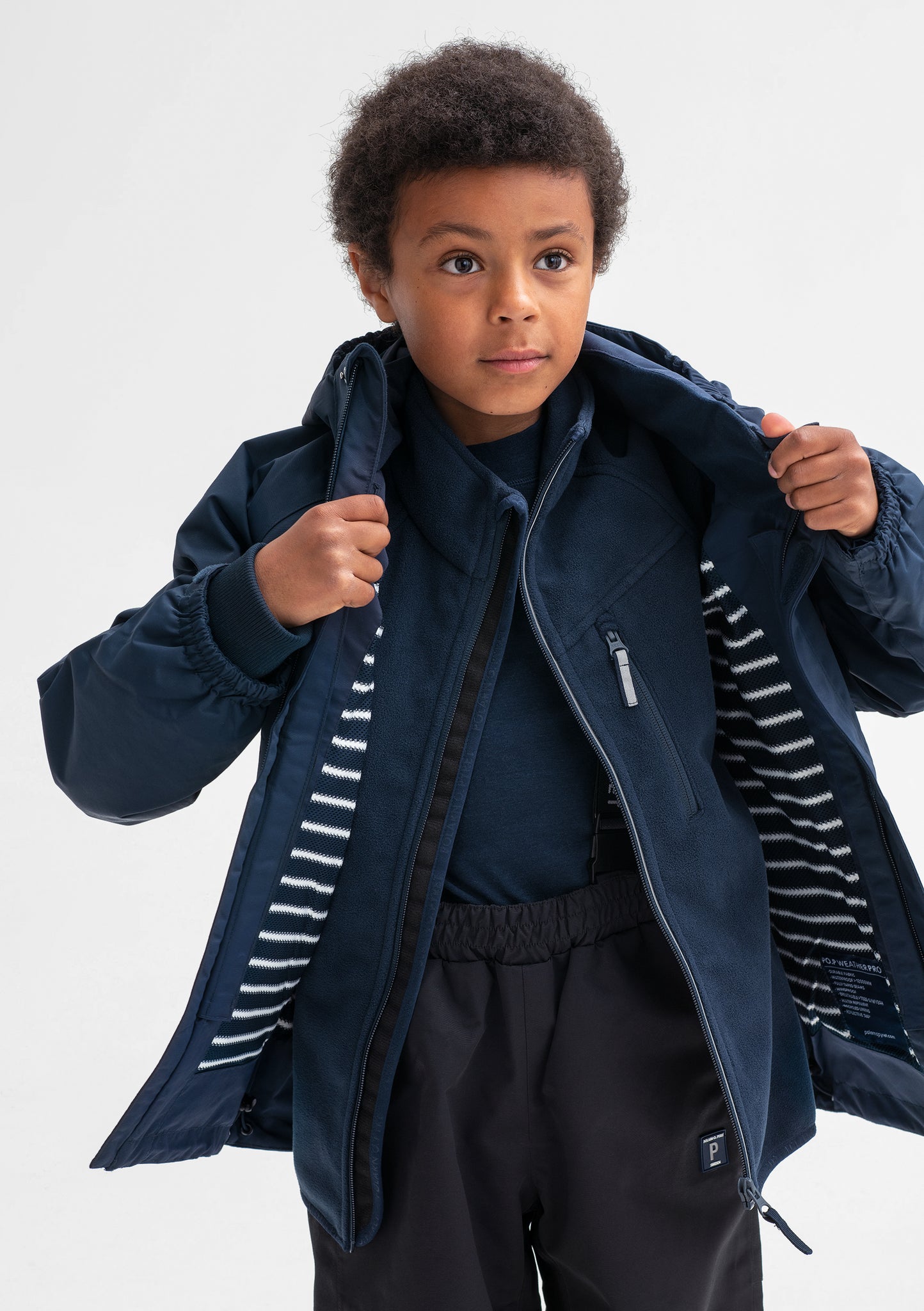 A little boy spotted wearing a navy, kids waterproof jacket, layered with navy, kids fleece jacket, made of soft fabric.